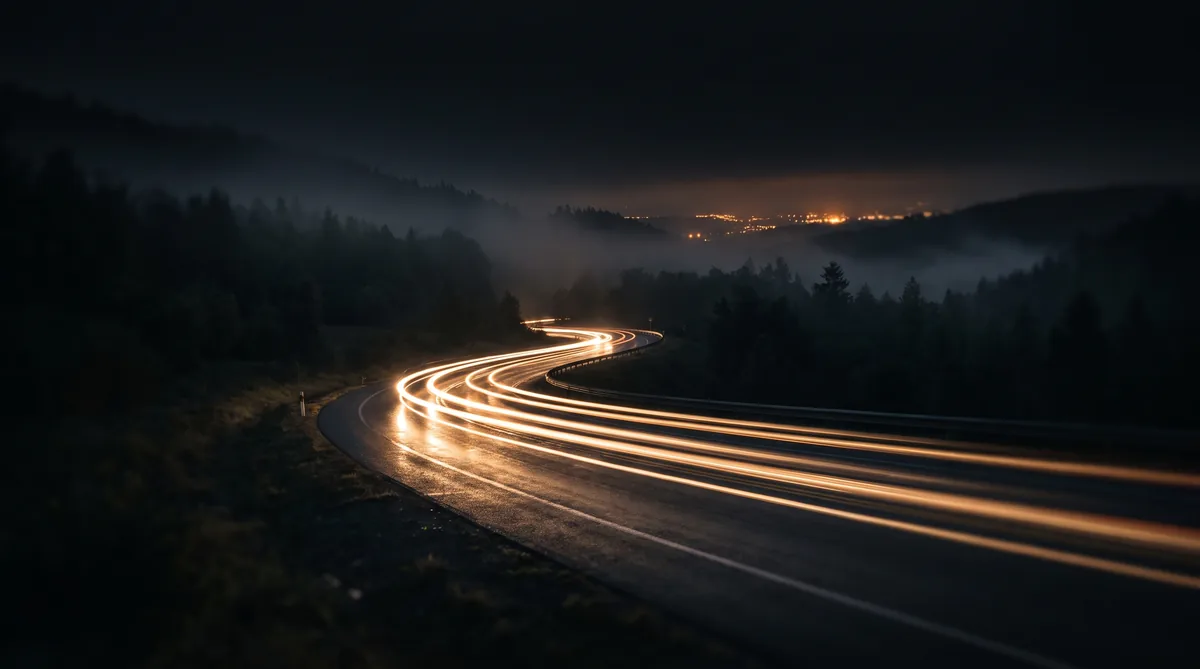 Landstraße im Sauerland bei Nacht, die Lichtspur eines Fahrzeugs zieht sich durch die Kurve